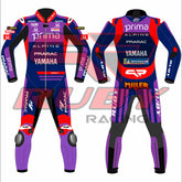 Front and rear views of the Prima Pramac Yamaha MotoGP 2025 racing suit for Jack Miller, displaying prominent sponsor logos such as Prima on the chest and back, along with Alpine, Pramac, and Yamaha. The suit is primarily blue with red and purple accents and includes the Ruby sponsor logo on the arms and legs. The back of the suit clearly shows the rider name "MILLER"