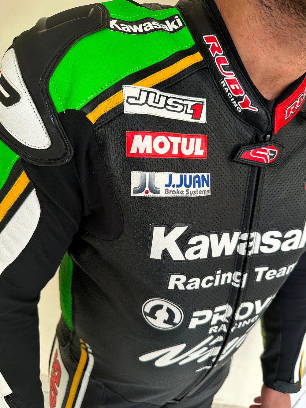 Closeup view of a Kawasaki Racing Team leather motorcycle suit highlighting detailed sponsor branding on the sleeves, aerodynamic padding, and reinforced knee protection.