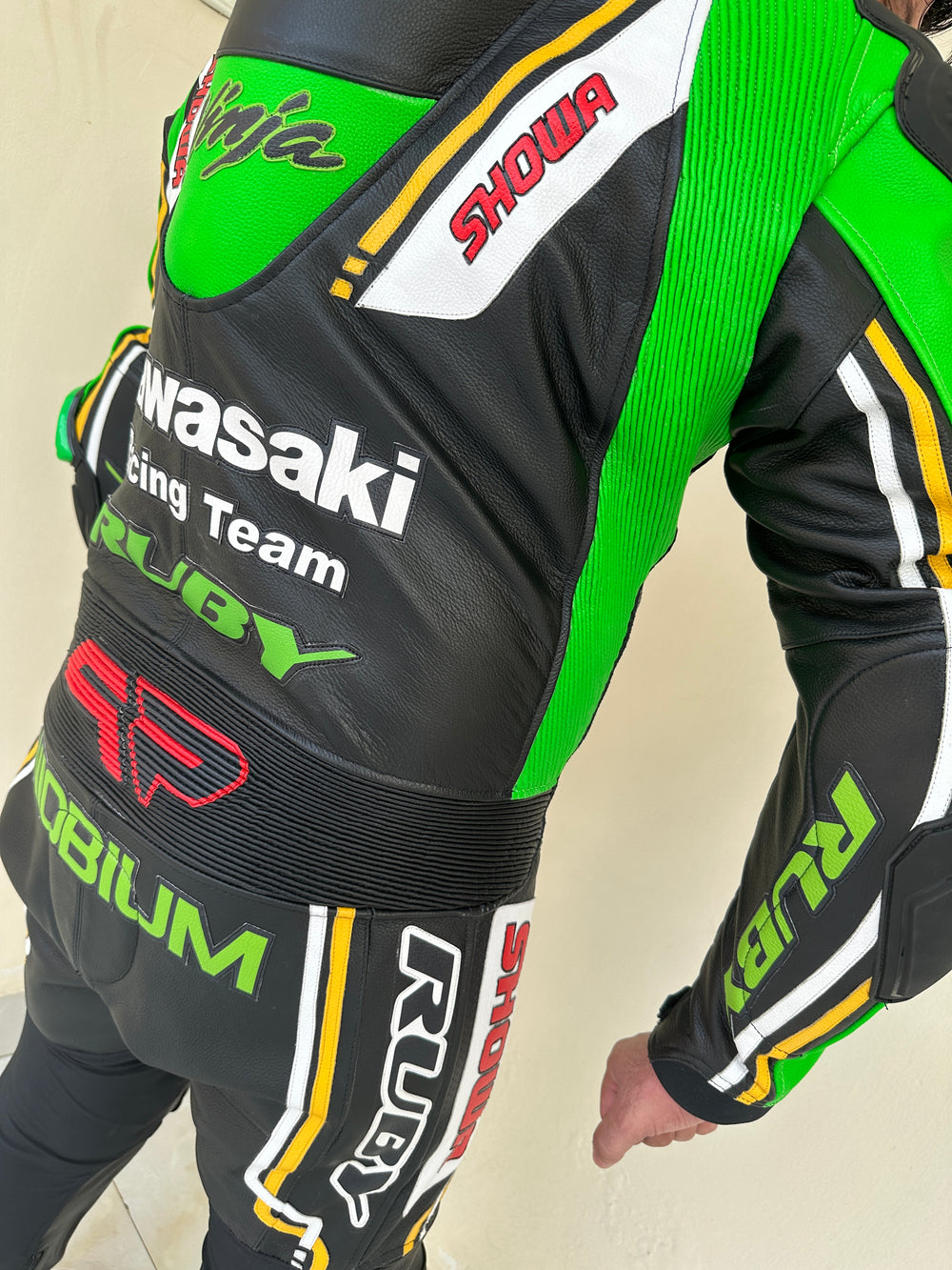 Closeup view of a Kawasaki Racing Team leather motorcycle suit highlighting detailed sponsor branding on the sleeves, aerodynamic padding, and reinforced knee protection.