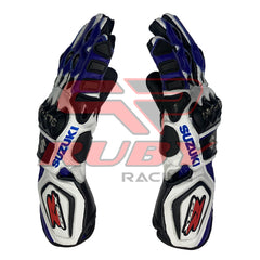 A pair of Suzuki GSXR motorcycle racing gloves shown from the side view. The gloves are predominantly blue, white, and black with red accents. They feature protective knuckle guards, reinforced palms, and finger protection. The Suzuki logo is visible on the wrist area. The gloves are high-performance gear designed for motorcycle racing.